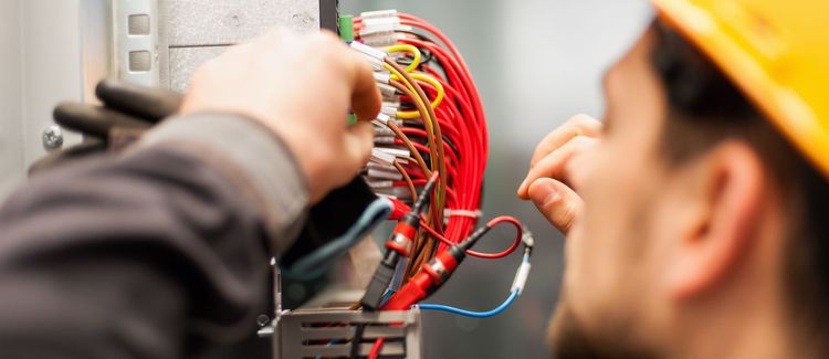 Technician wiring a red electrical panel with colorful cables in a workspace.
