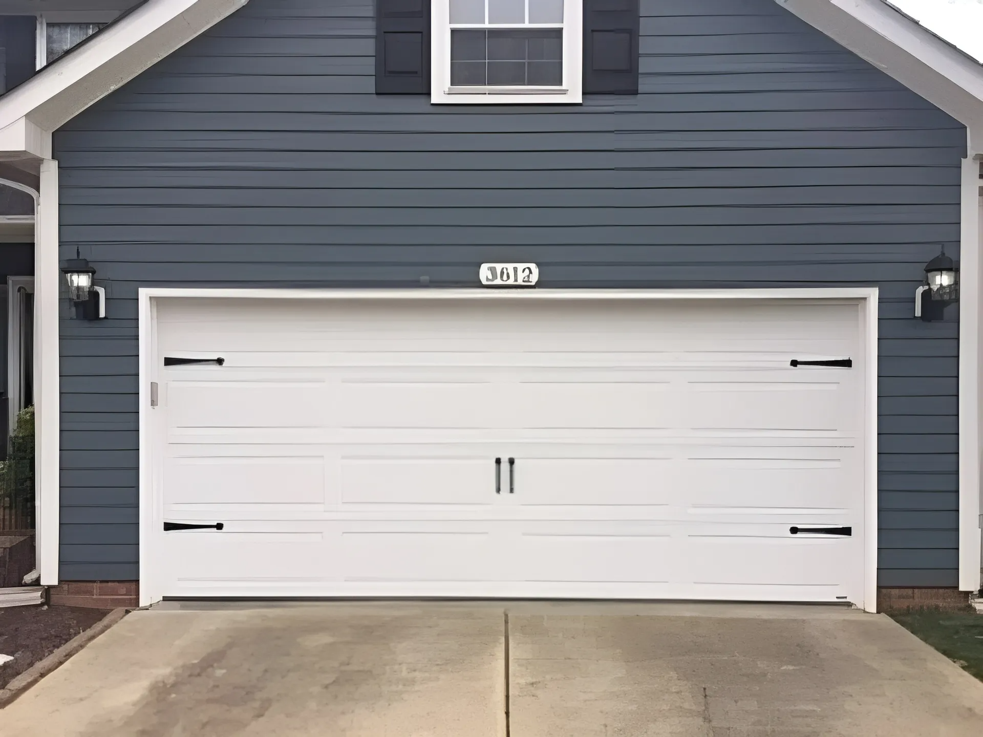 White garage door with black hardware on a blue house.