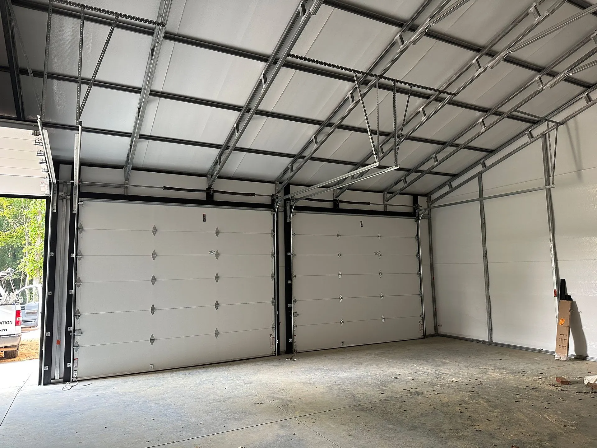 Interior of a metal building with two large garage doors, light gray walls, and a concrete floor.