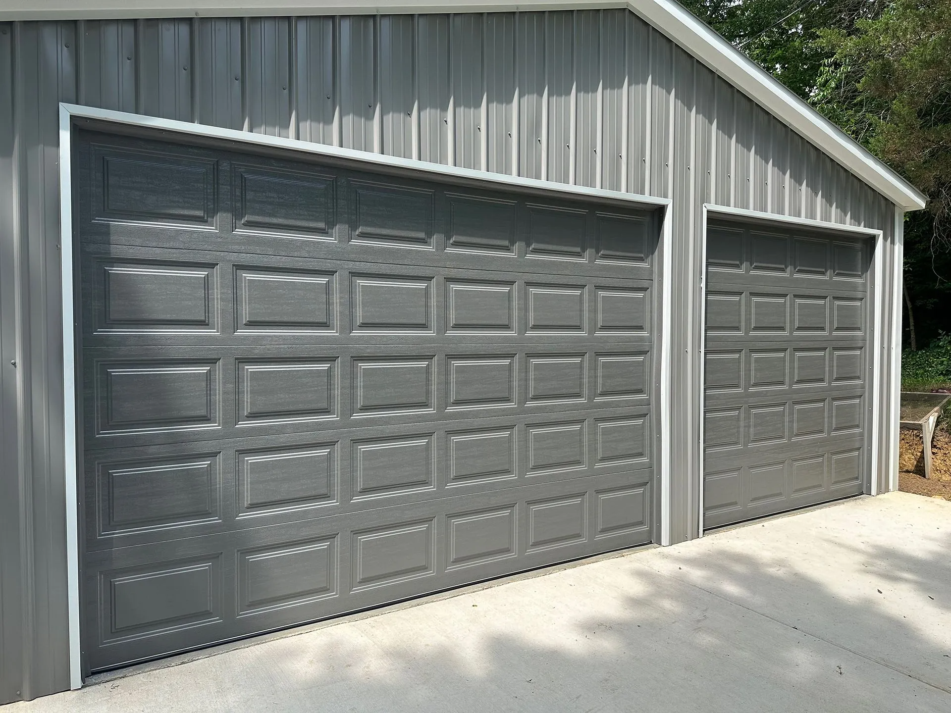 Gray metal garage with two doors, white trim, set against a gray metal building.