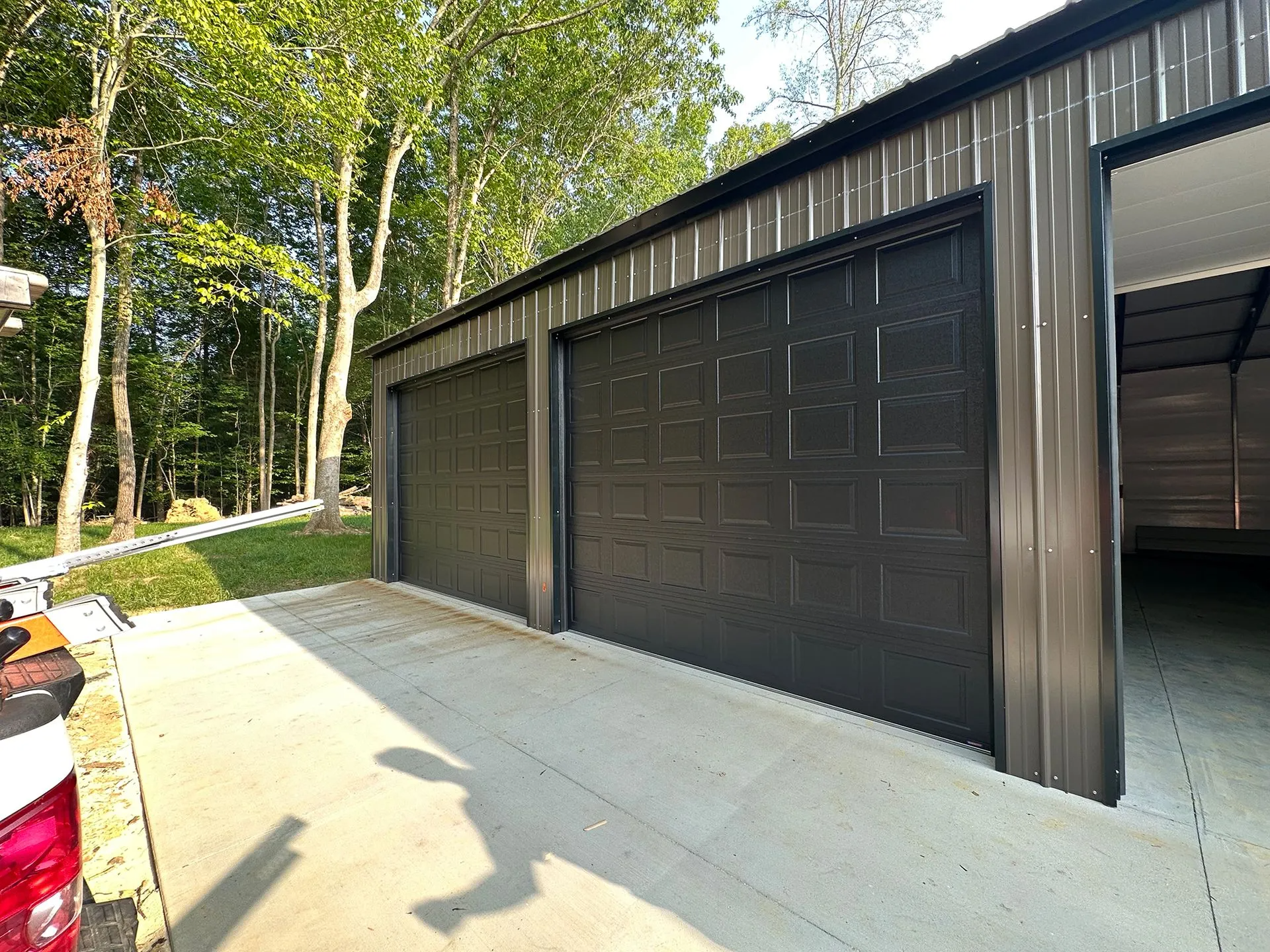 Dark gray garage with three bays and black doors in a wooded setting.