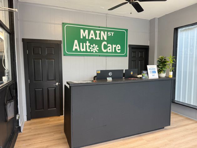 Main St Auto Care reception desk with green sign, black doors, and a potted plant in a gray lobby