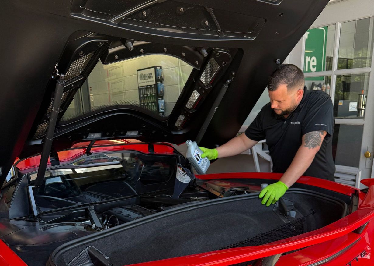 Mechanic inspecting a red sports car with the rear hatch open in a garage