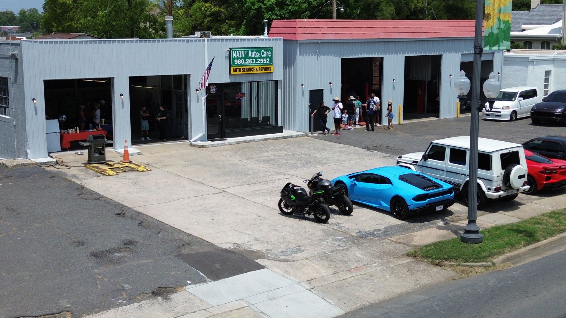 Auto repair shop exterior with motorcycles, a blue sports car, and parked vehicles in the lot.