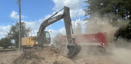 A yellow excavator is removing a tree stump from the ground.