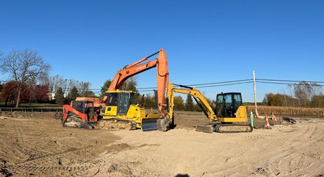 A yellow excavator is demolishing a building in a construction site.