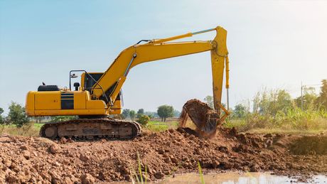A yellow excavator is digging a hole in the dirt in a field.