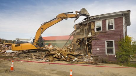 A yellow excavator is demolishing a red house.