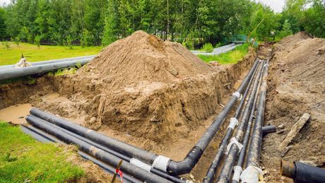 A bunch of pipes are laying in the dirt in a trench.