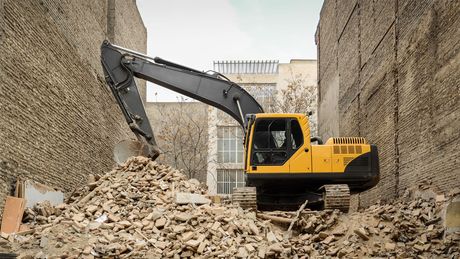 A yellow excavator is demolishing a building in a construction site.