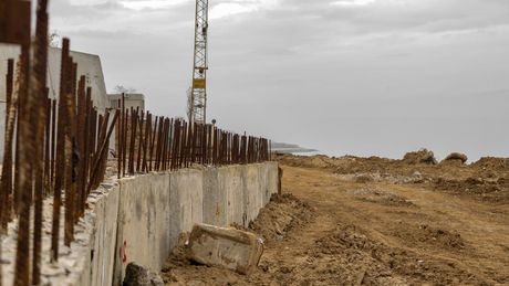 A concrete wall is being built in a dirt field with a crane in the background.