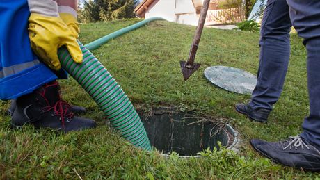 A man is pumping water into a septic tank with a green hose.