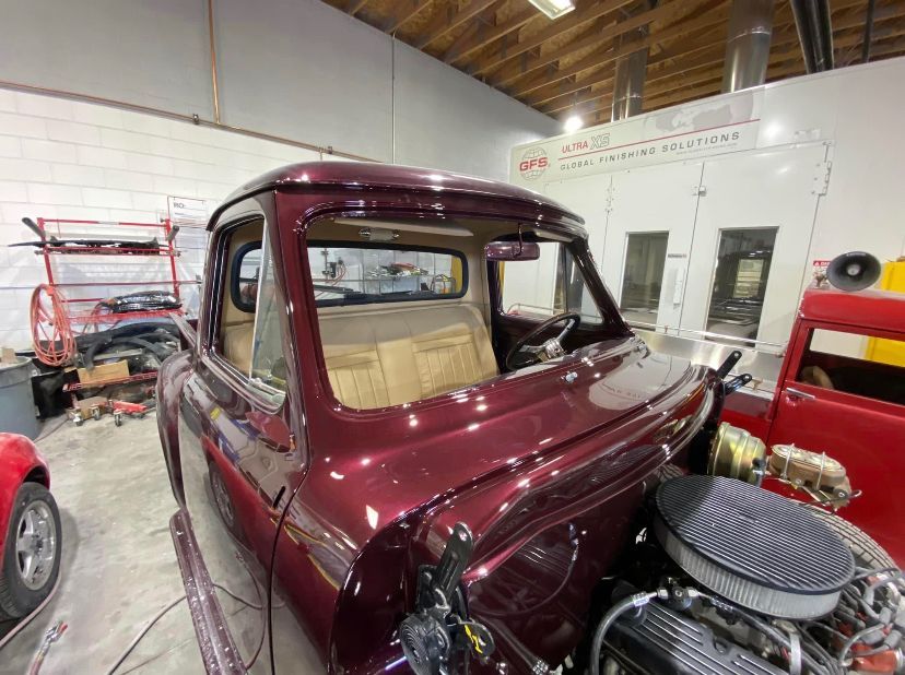 A purple truck is sitting in a garage next to a red truck before