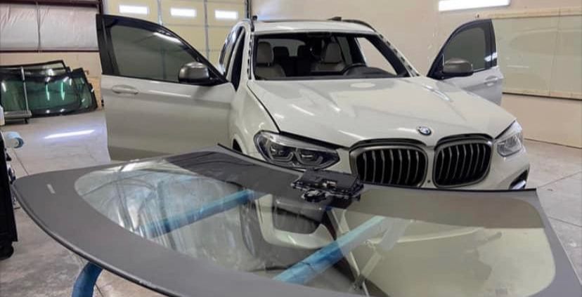 A white bmw x3 is sitting in a garage with its windshield being replaced