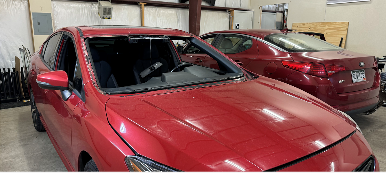 A red car with a broken windshield is parked in a garage.