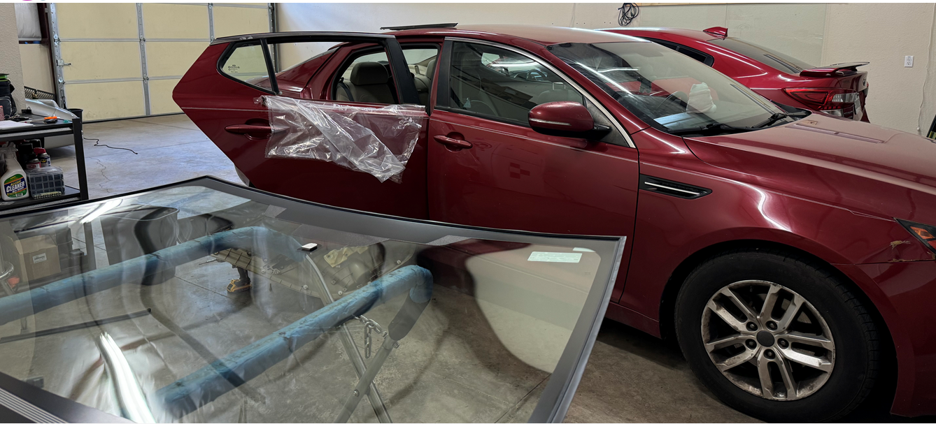 A red car is sitting in a garage with a windshield missing.