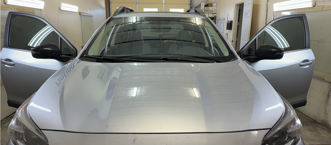 A silver car is parked in a garage with its doors open.