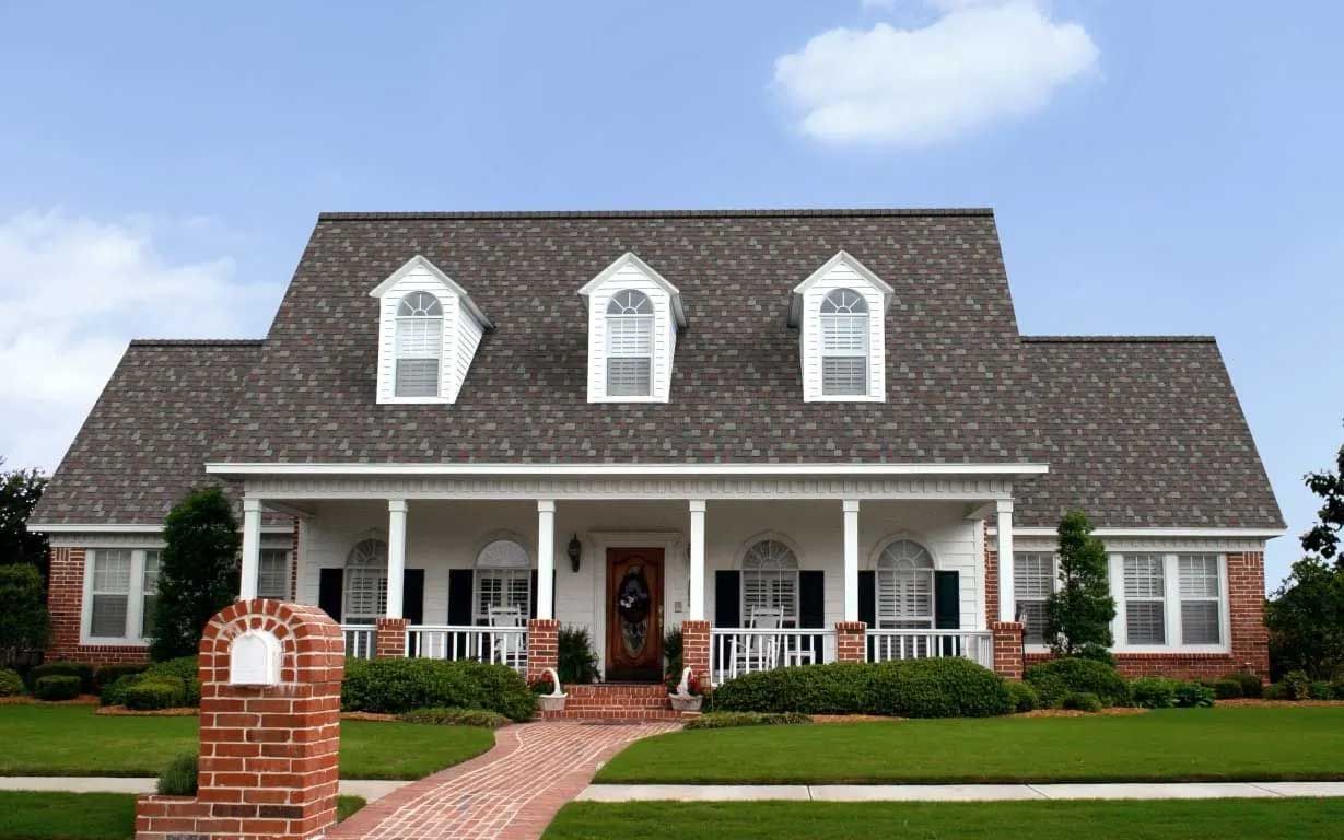 Brick house with white porch, brick walkway, and green lawn under a blue sky.