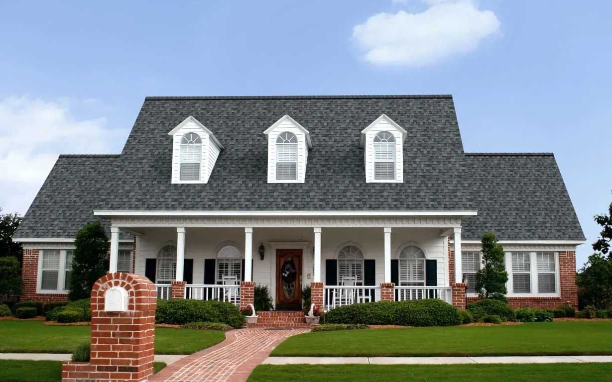 A two-story house with a porch, brick pathway, and dormer windows against a blue sky.