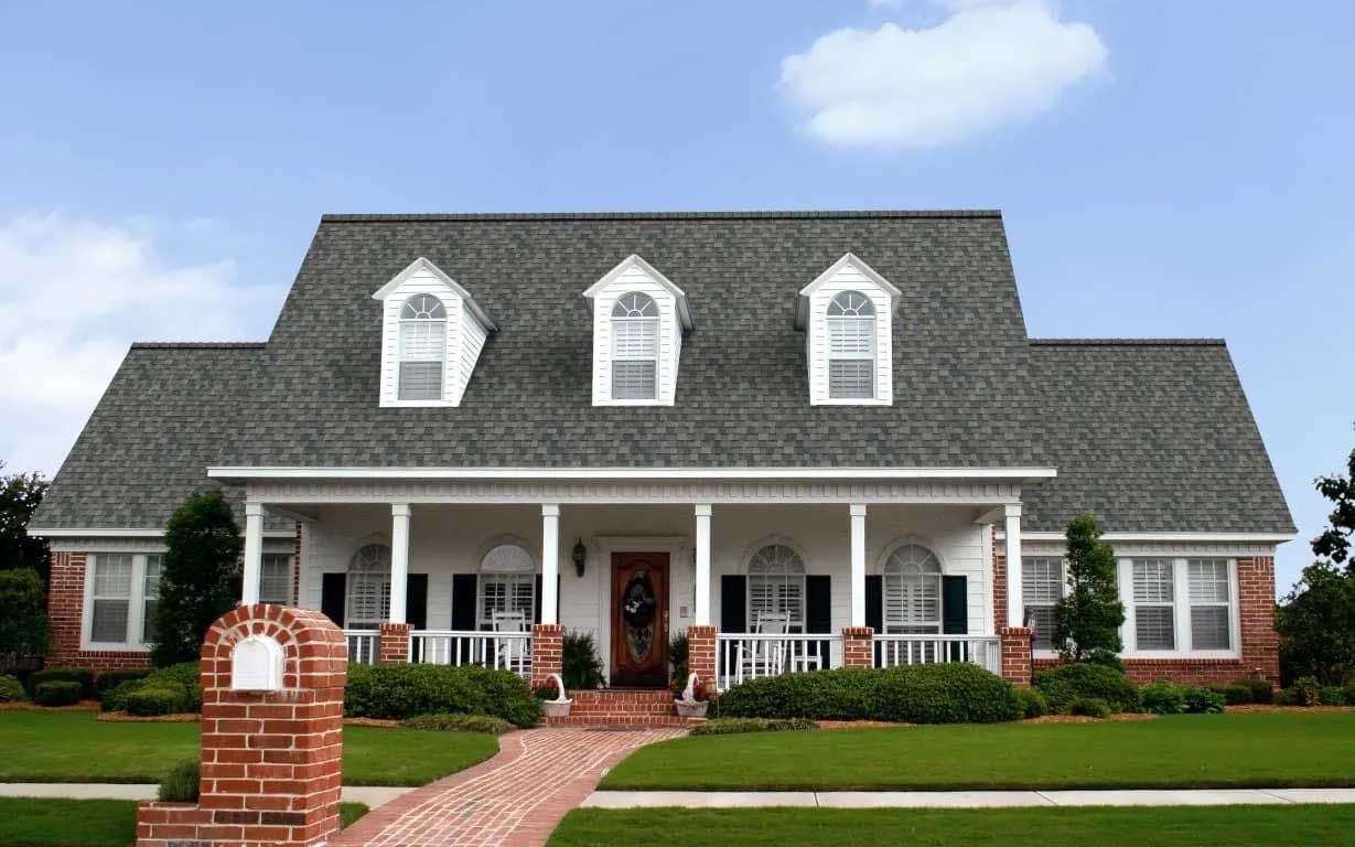 Two-story house with a porch, dormers, and a brick pathway.