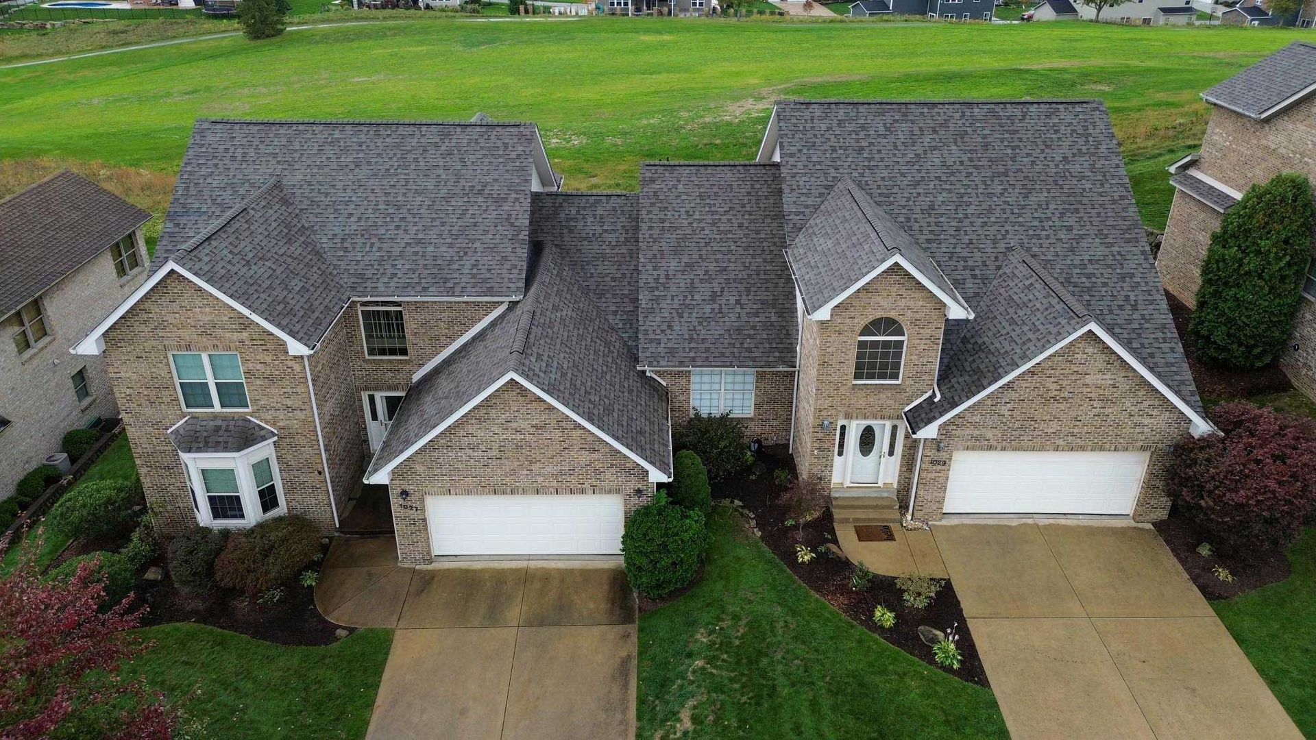 Two-story brick houses with gray roofs. Each has a two-car garage. Set on a green lawn.