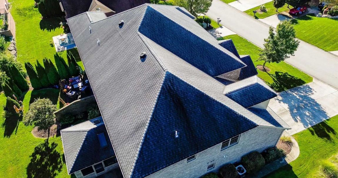 Overhead view of a house with a dark gray roof surrounded by green grass and a street.