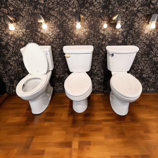 Three toilets are lined up next to each other on a wooden floor