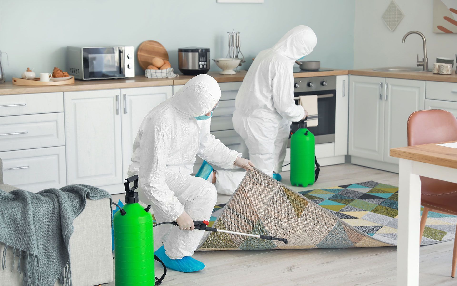 Two people in white protective suits cleaning a kitchen floor with green cleaning canisters
