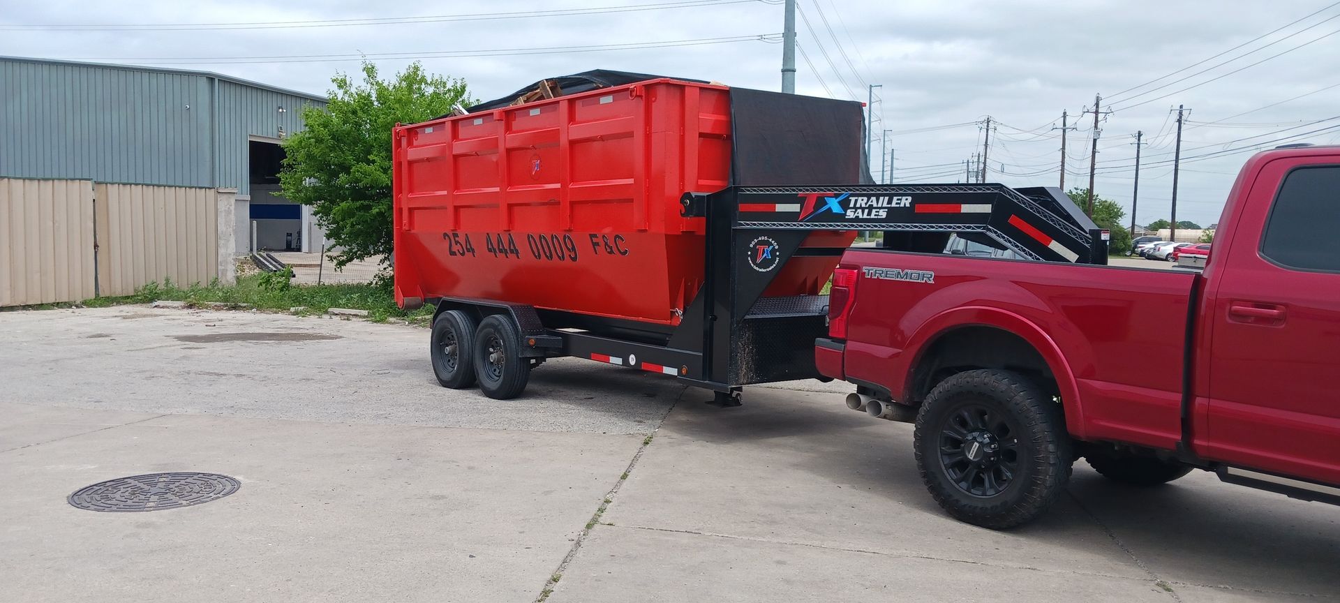 Red pickup truck towing a red dumpster trailer on a concrete surface.