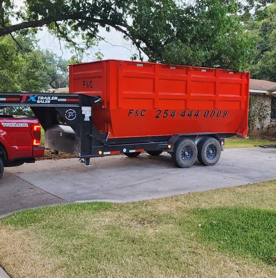 Red dumpster trailer attached to a red truck on a driveway. The trailer has the phone number 254-444-0009.