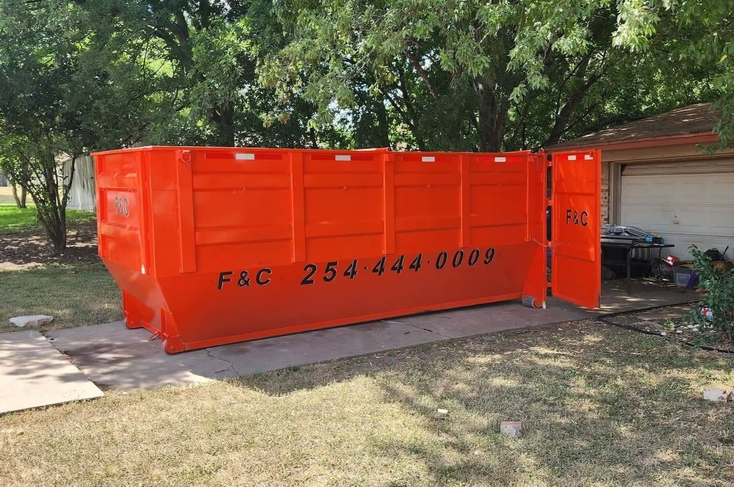 Bright orange dumpster on a concrete slab, with F&C and phone number 254-444-0009 visible.