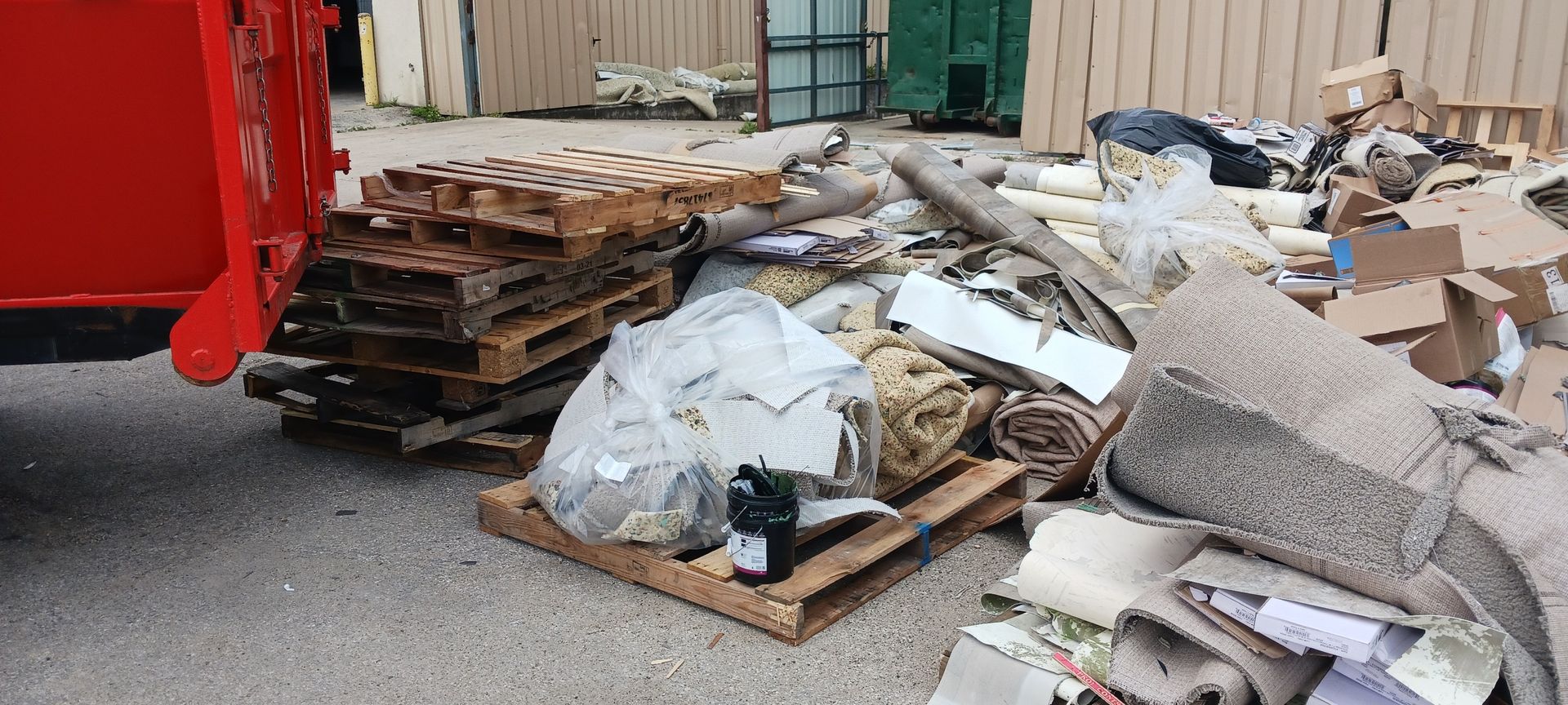 Pile of trash and pallets next to a red dumpster.