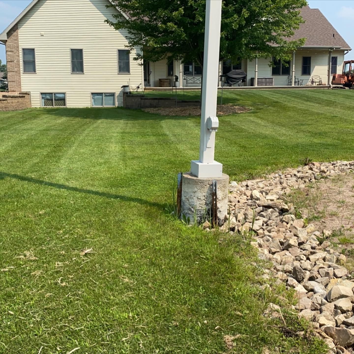 A white pole is in the middle of a lush green lawn in front of a house.
