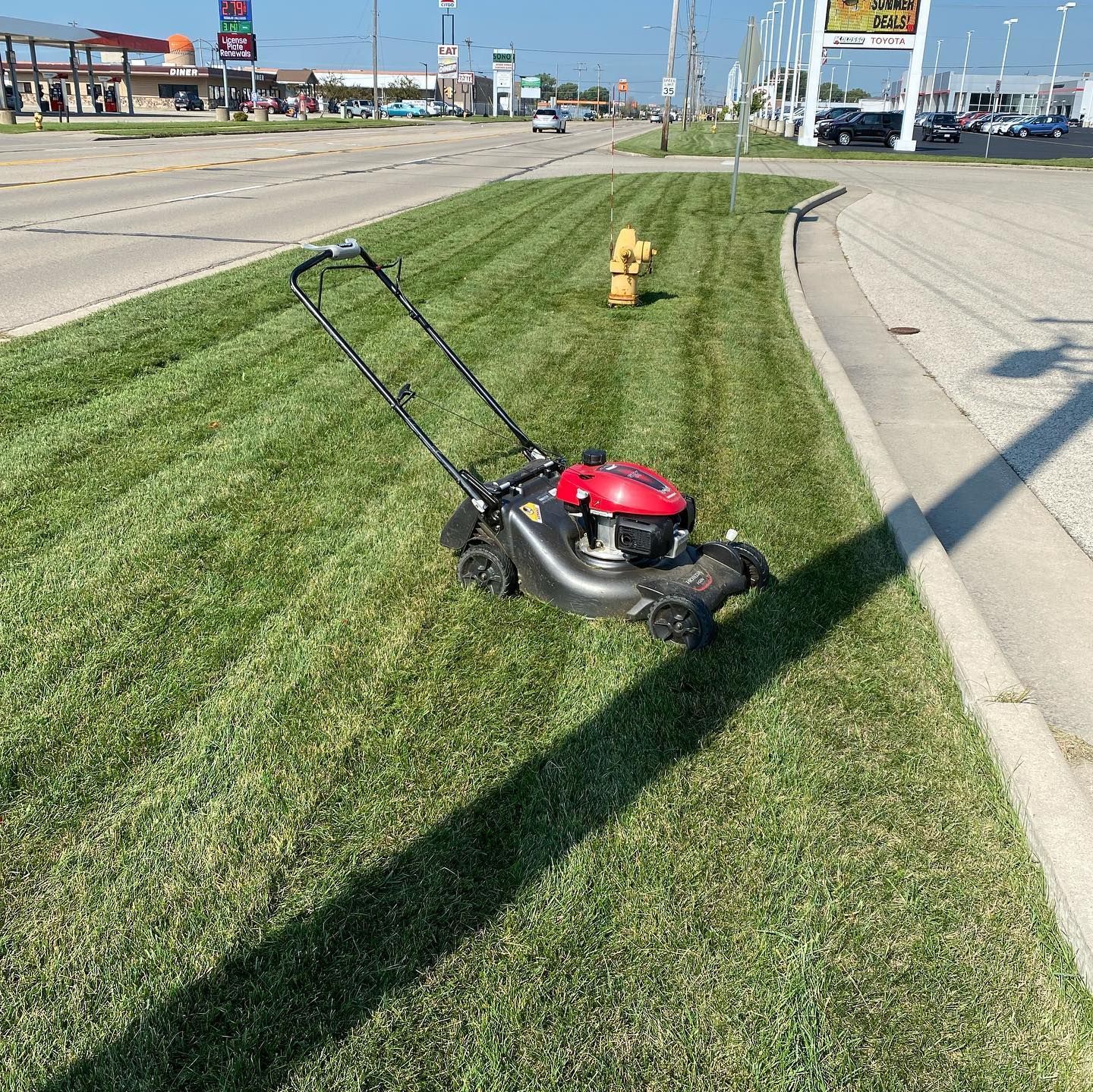 A lawn mower is sitting on top of a lush green lawn next to a fire hydrant.