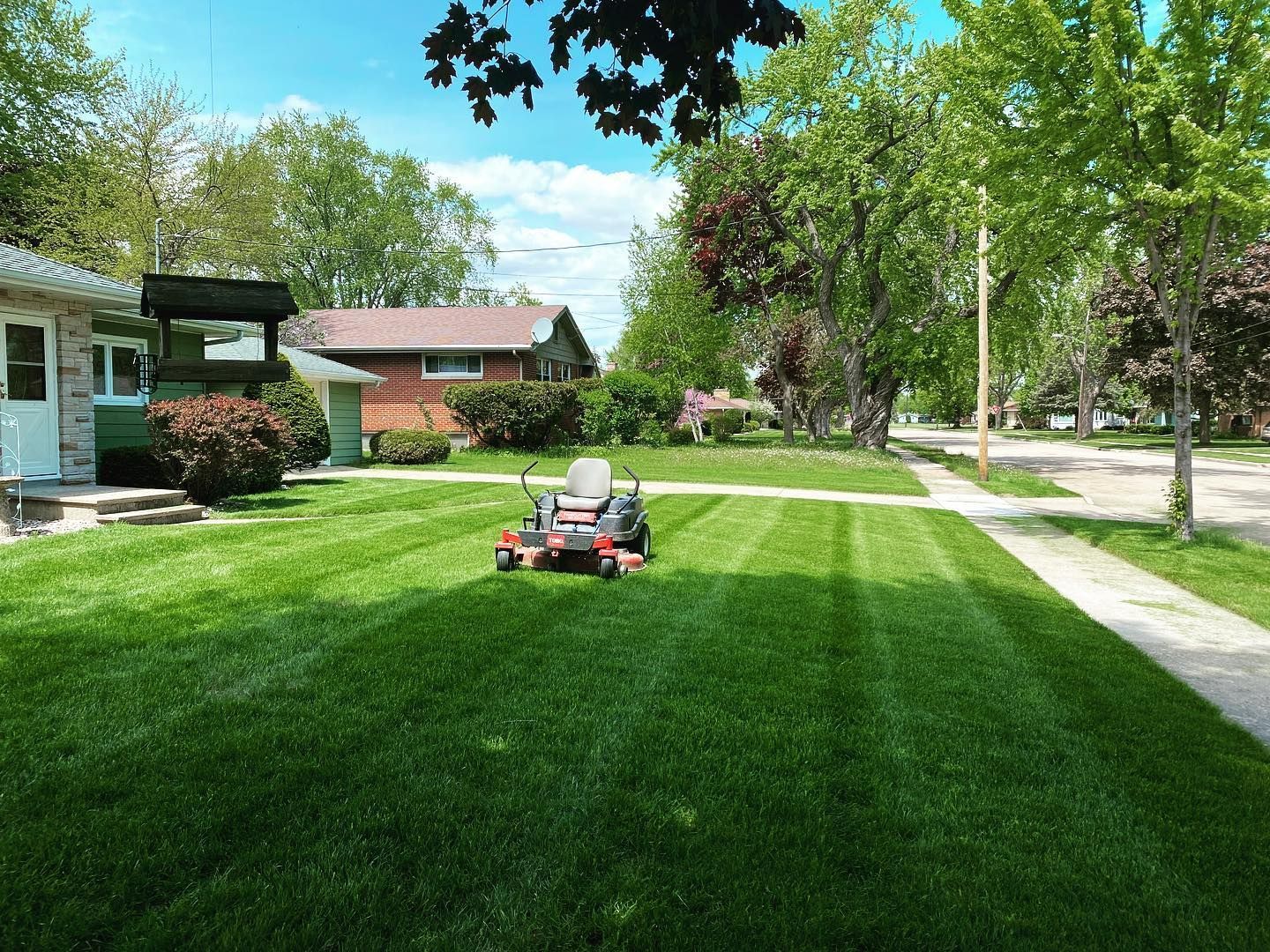 A lawn mower is cutting a lush green lawn in front of a house.