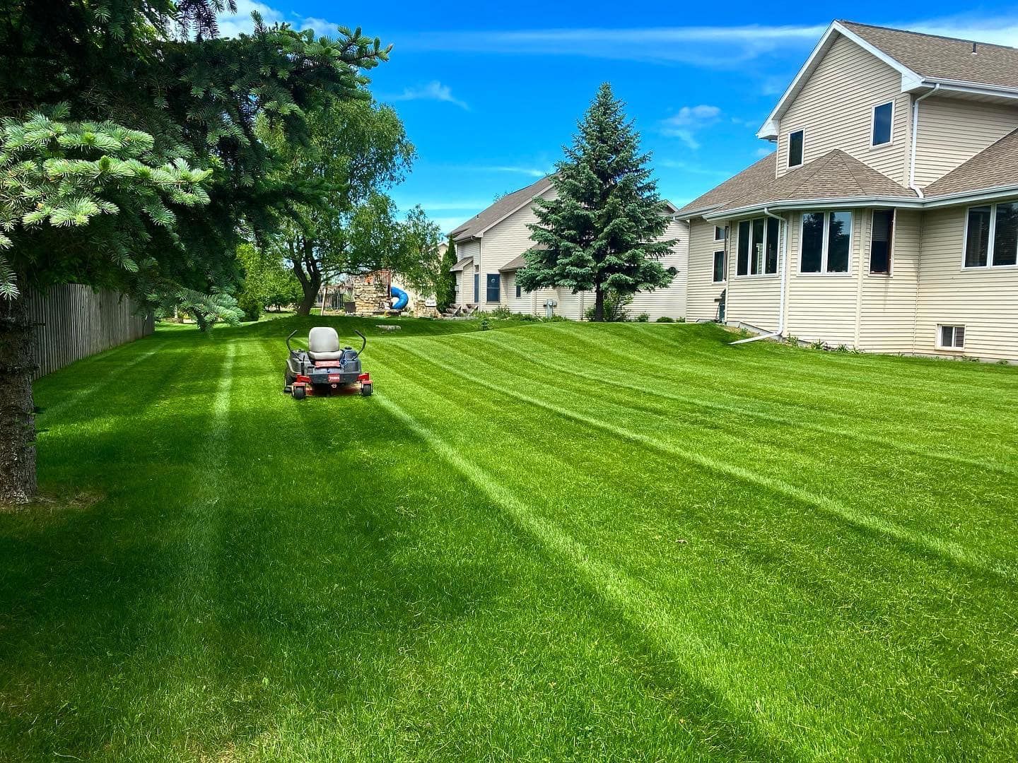 A person is riding a lawn mower on a lush green lawn in front of a house.