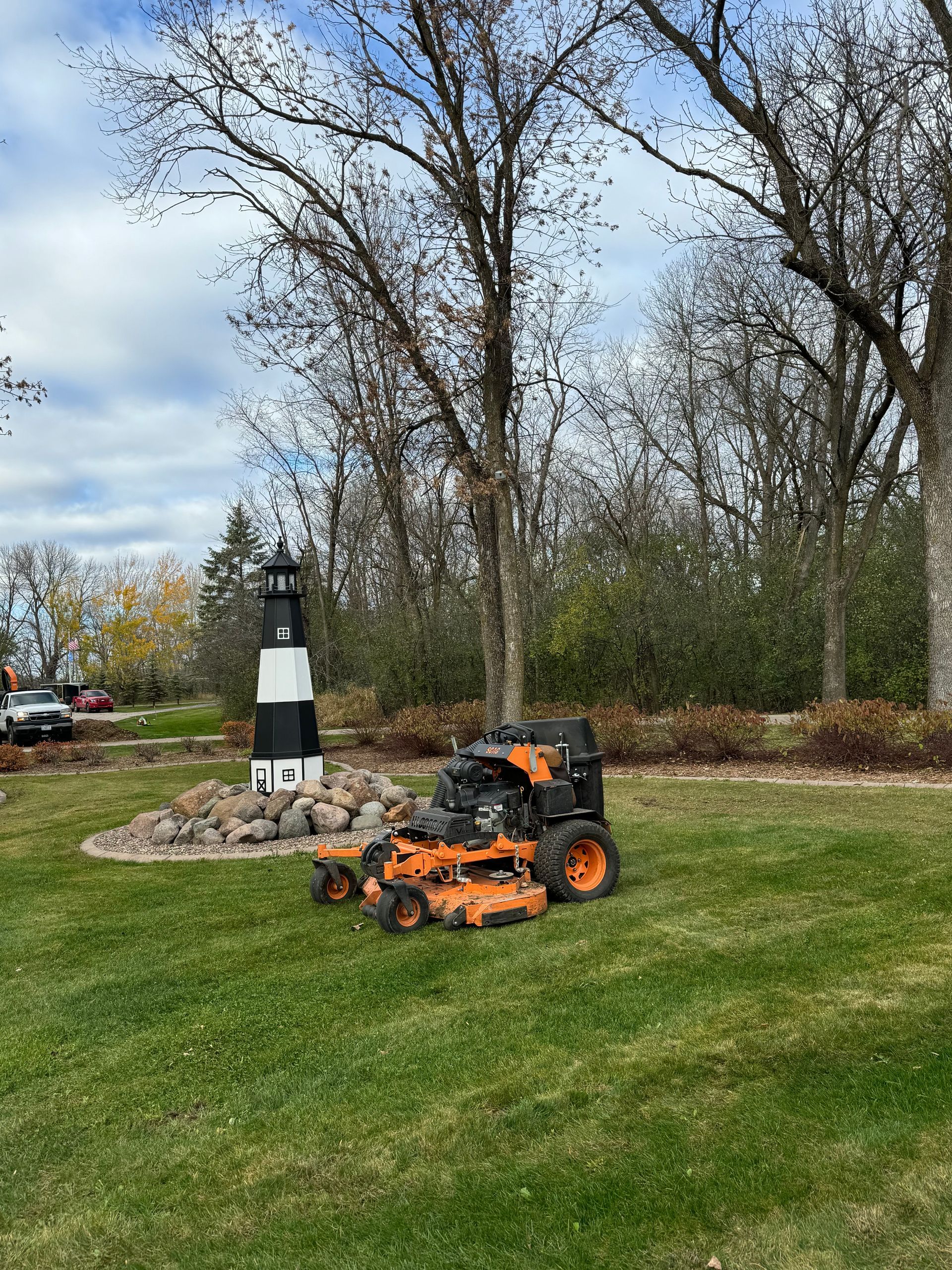 A lawn mower is sitting on top of a lush green lawn next to a lighthouse.