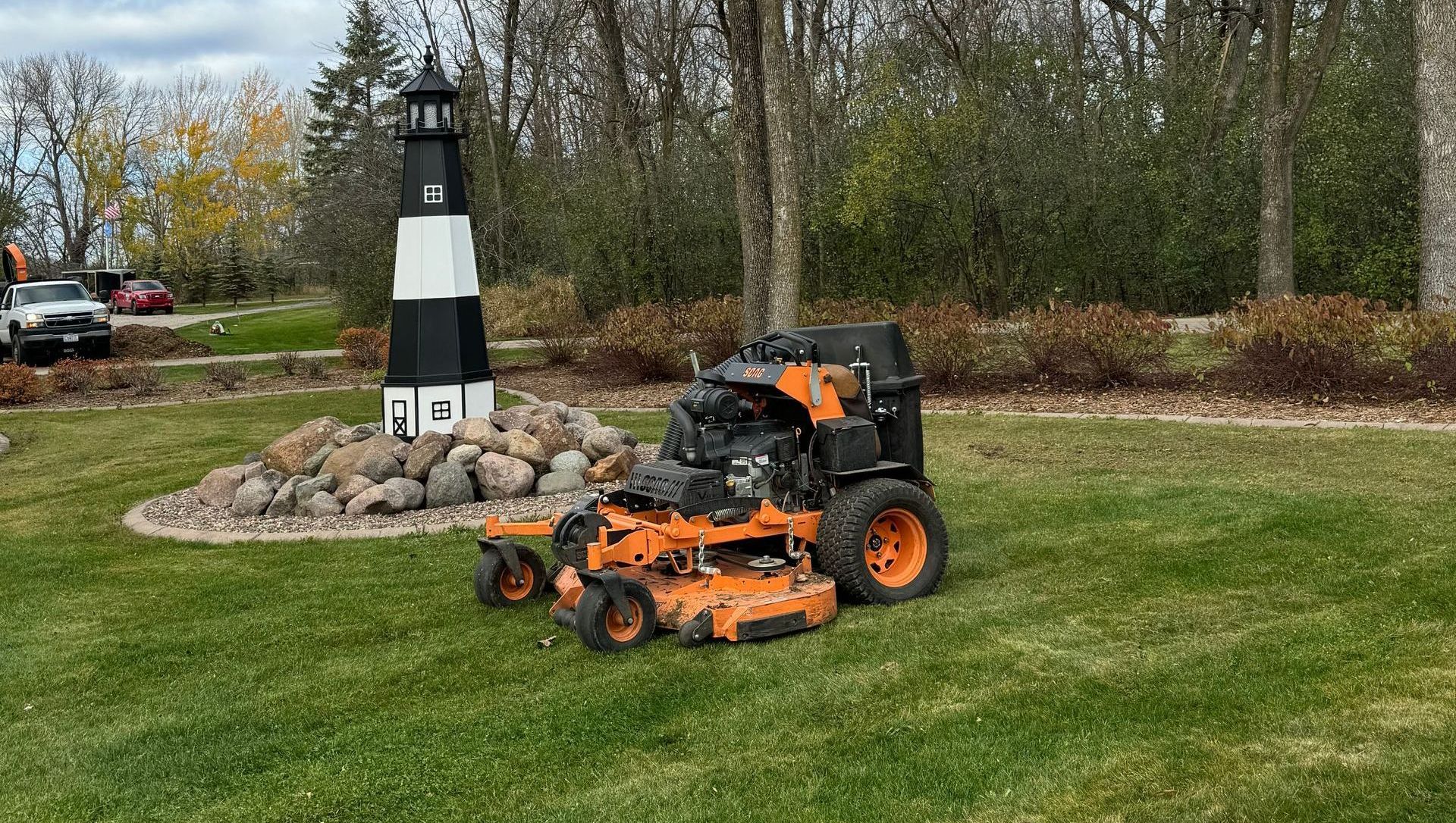A lawn mower is cutting a lush green lawn next to a lighthouse.
