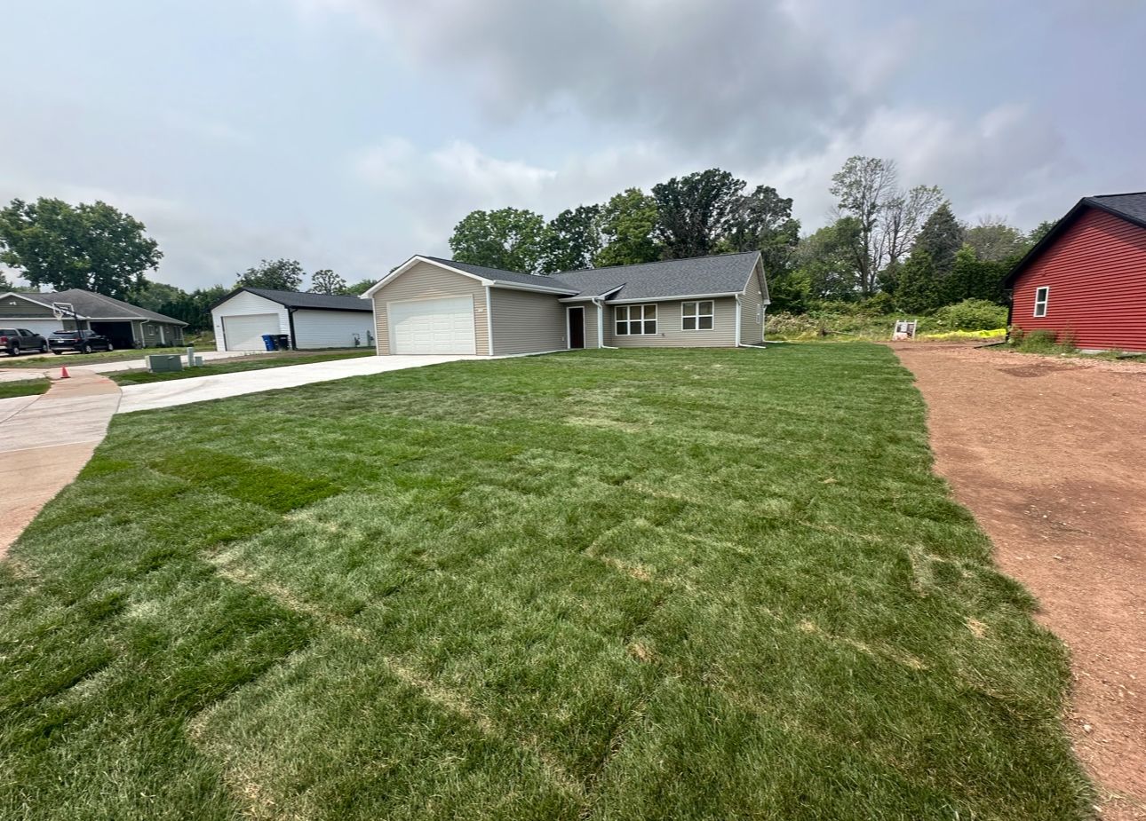 A house with a large lawn in front of it and a red barn in the background.