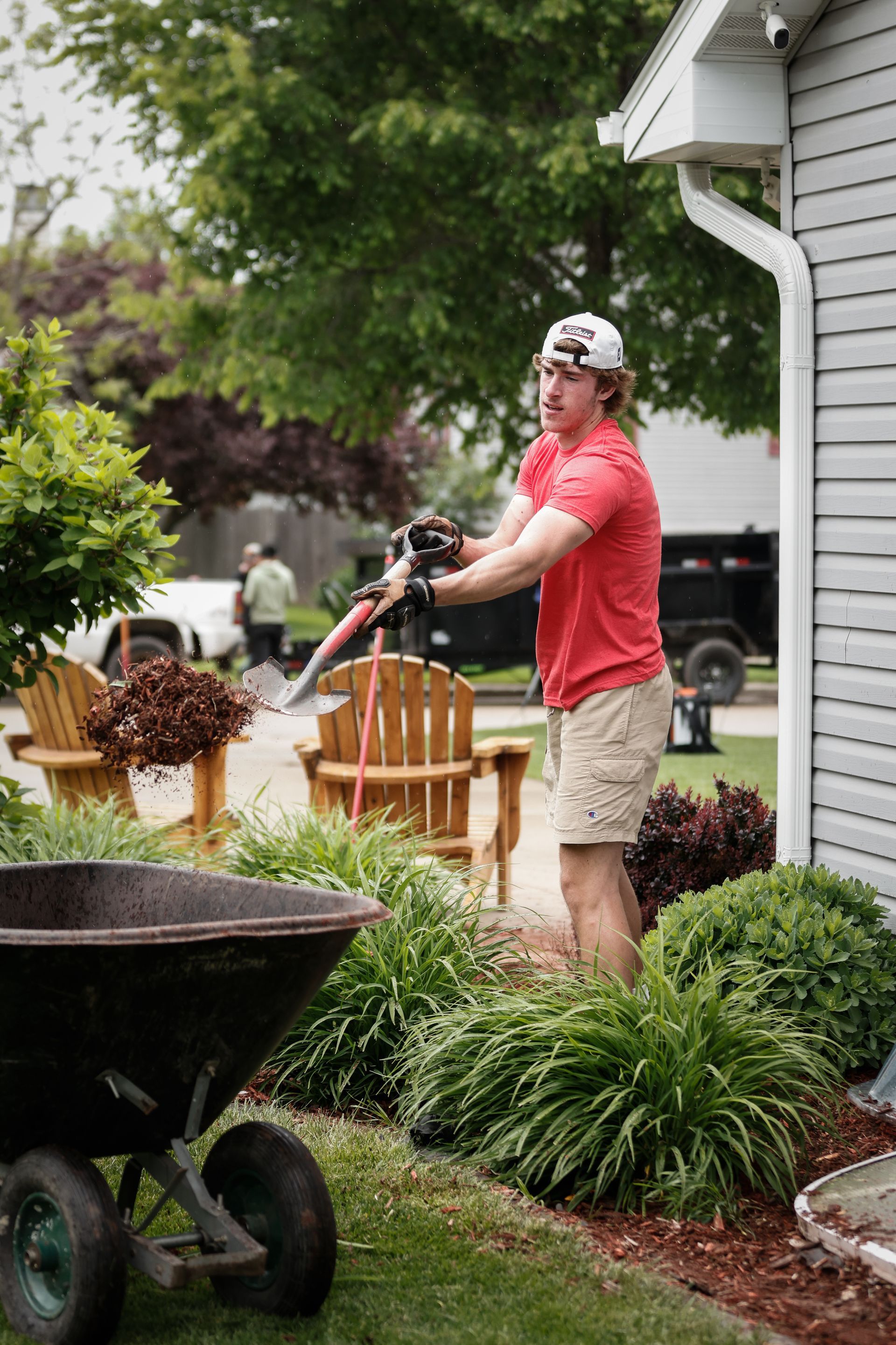 A man is standing next to a wheelbarrow in front of a house.