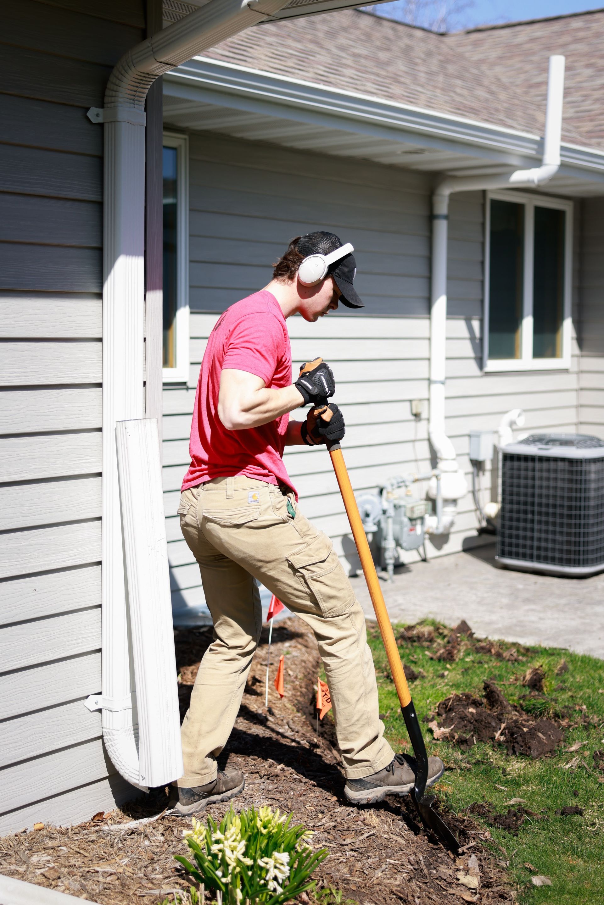 A man is digging a hole in the ground in front of a house with a shovel.