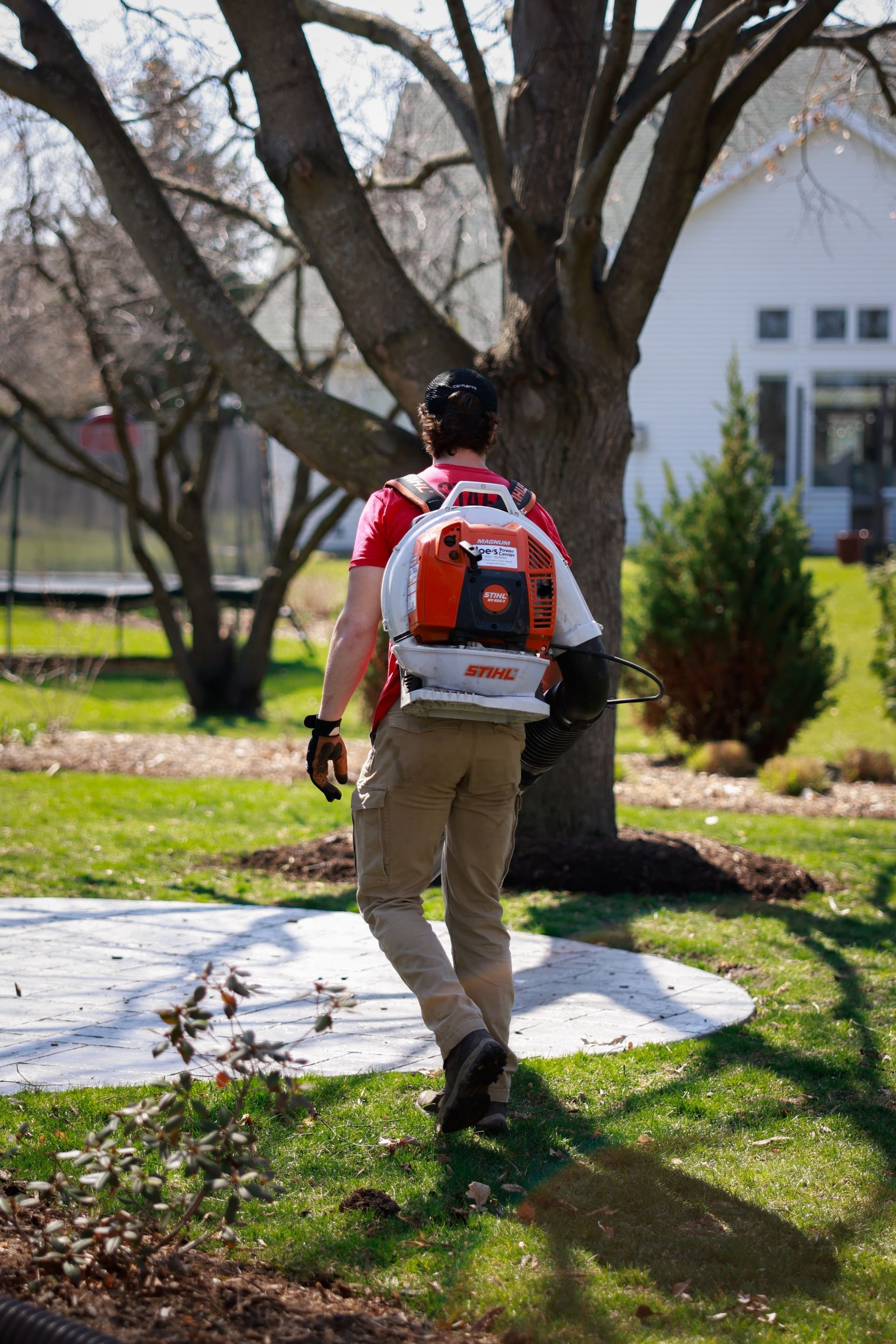 A man is walking in a yard with a backpack on his back.