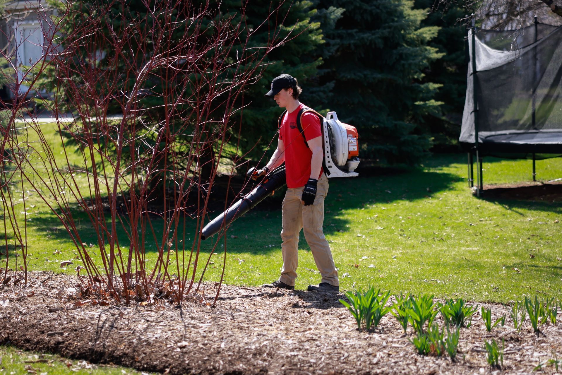 A man is blowing leaves in a garden with a backpack.