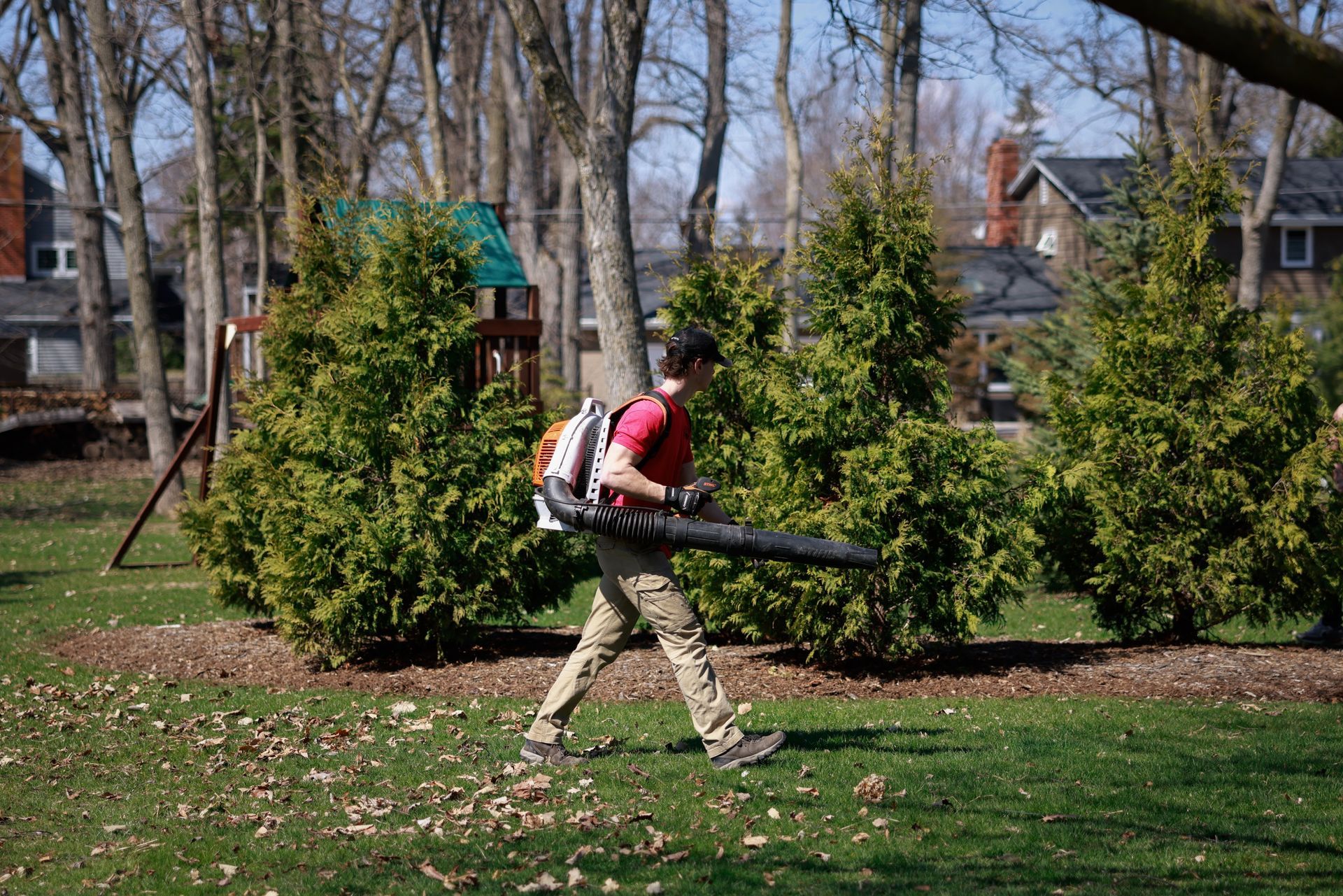A man is blowing leaves in a park with a backpack.