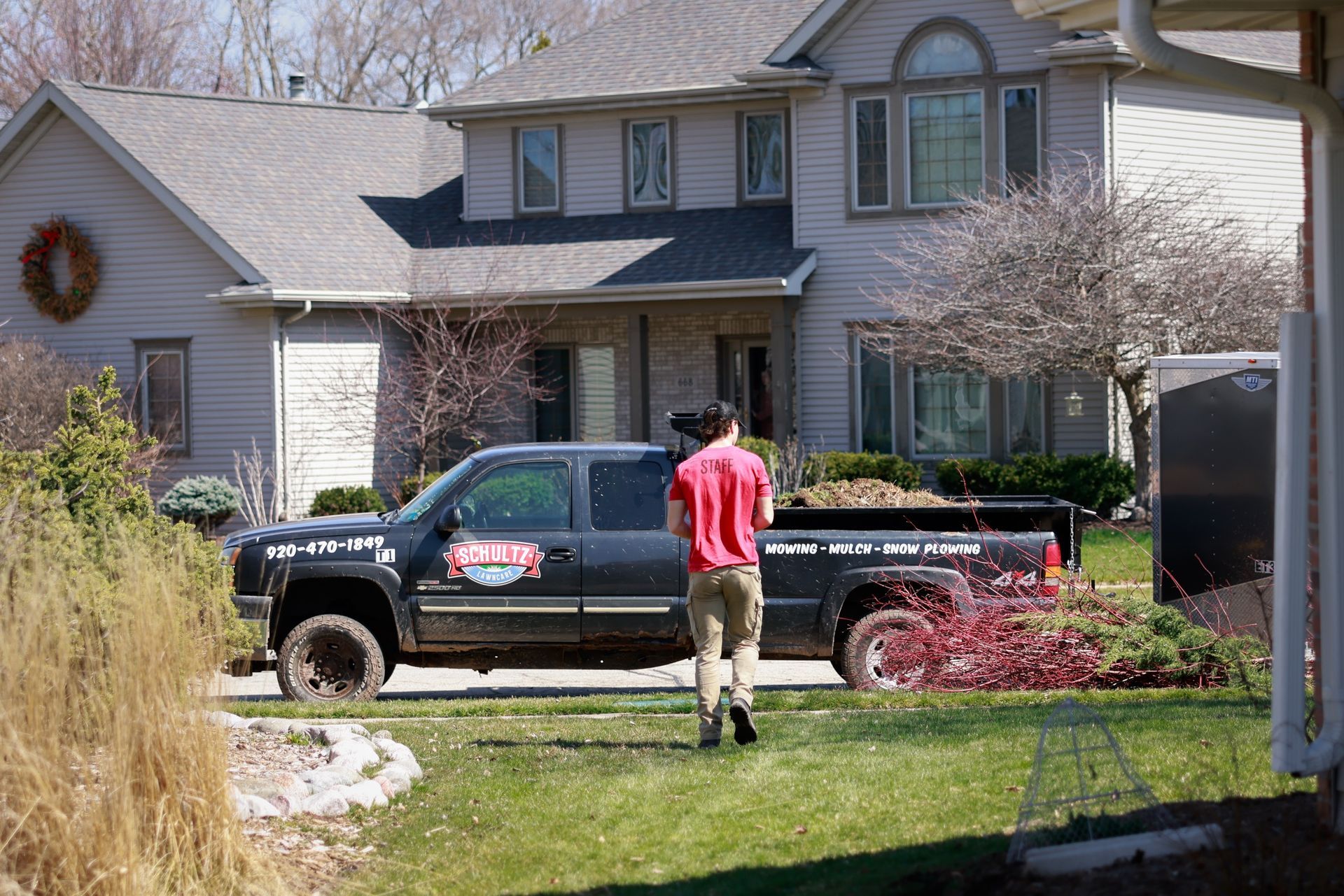 A man in a red shirt is standing in front of a truck that says ' lawn care ' on it