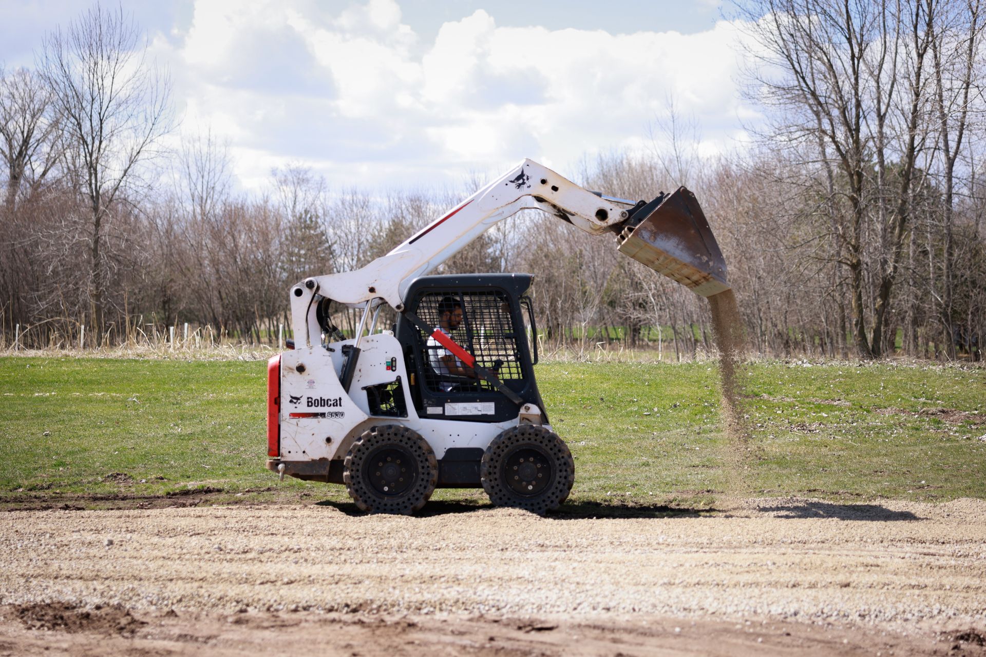 A man is driving a bobcat loader in a field.