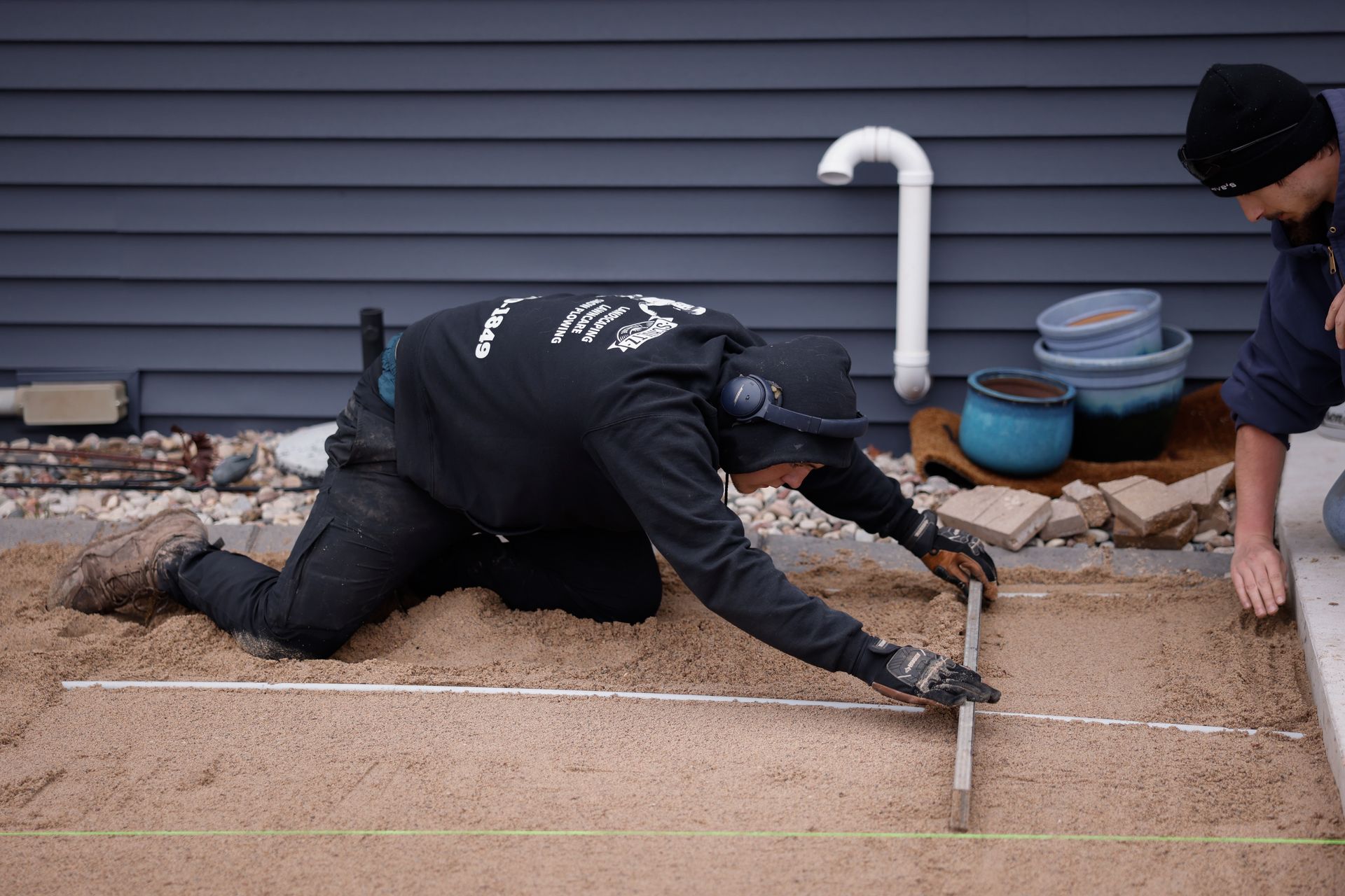 A man is kneeling on the ground using a tape measure.