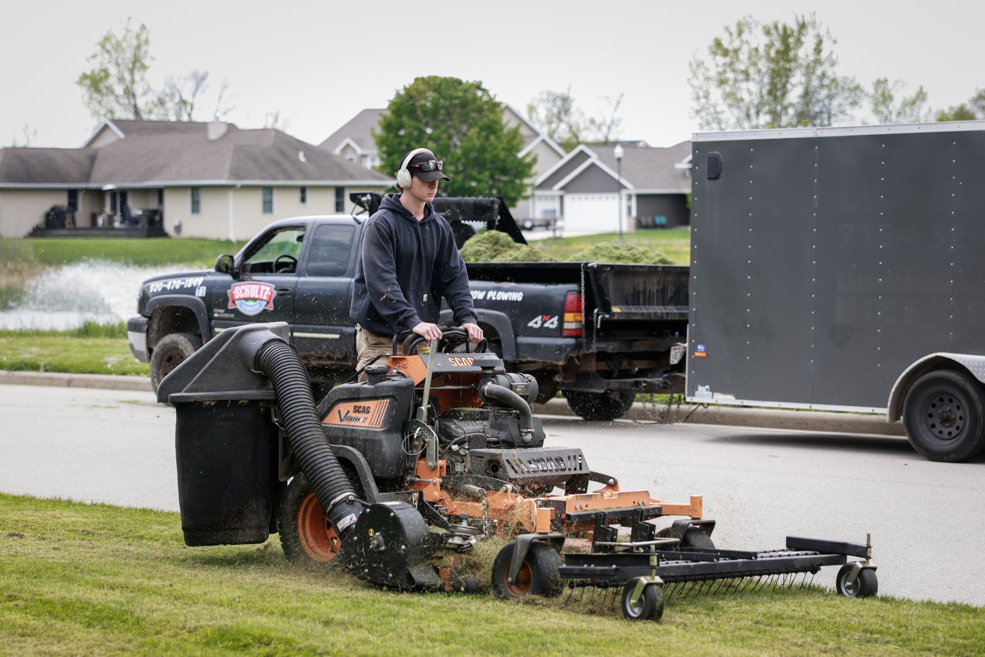 A man is riding a lawn mower next to a trailer.