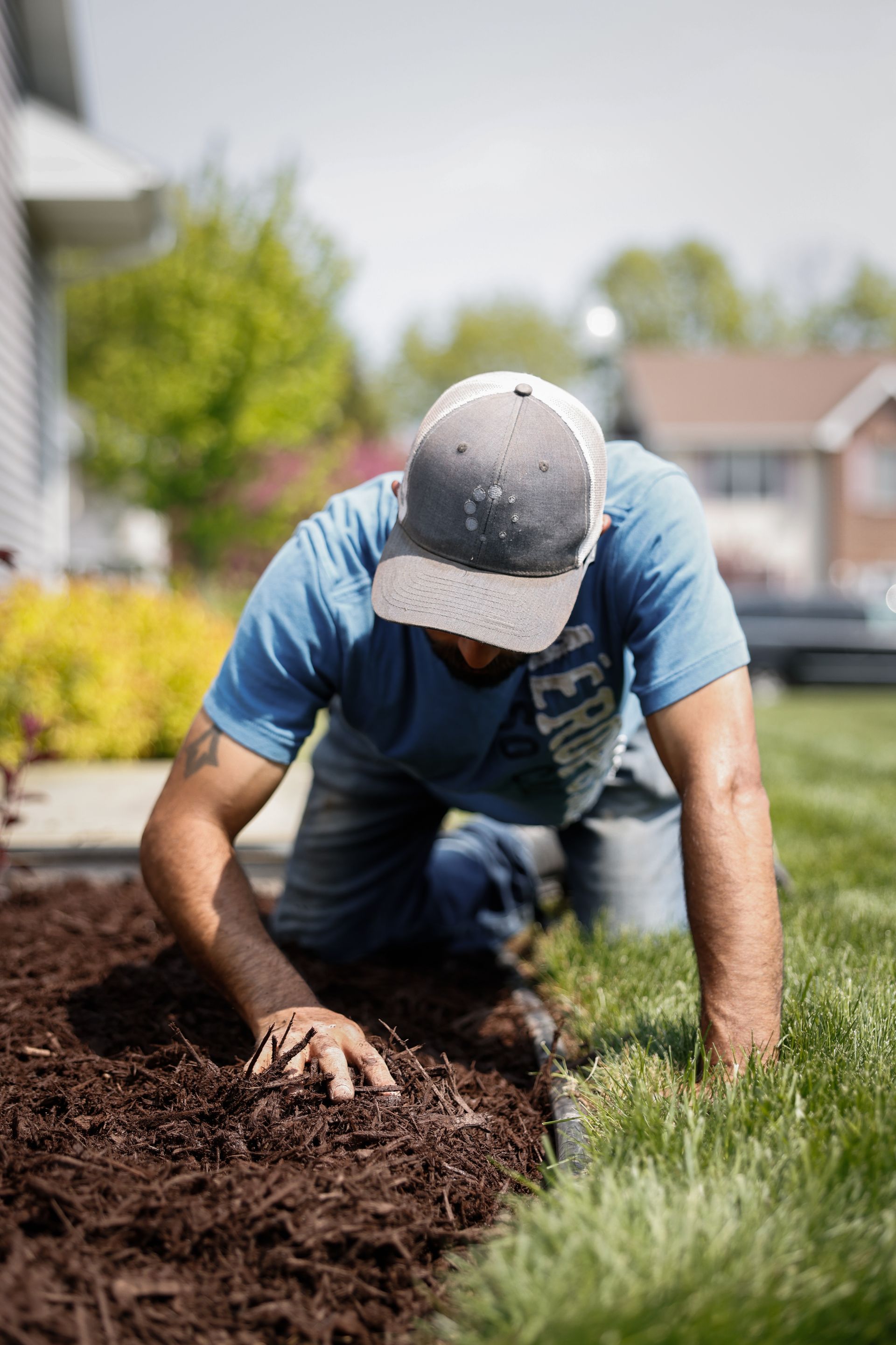 A man is kneeling down in the dirt in a yard.