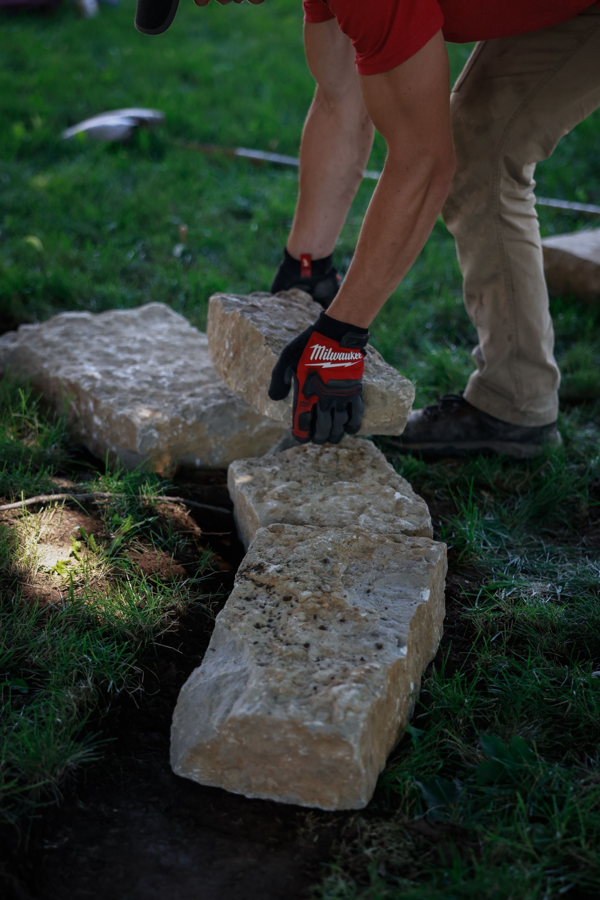A person is laying bricks in the grass.